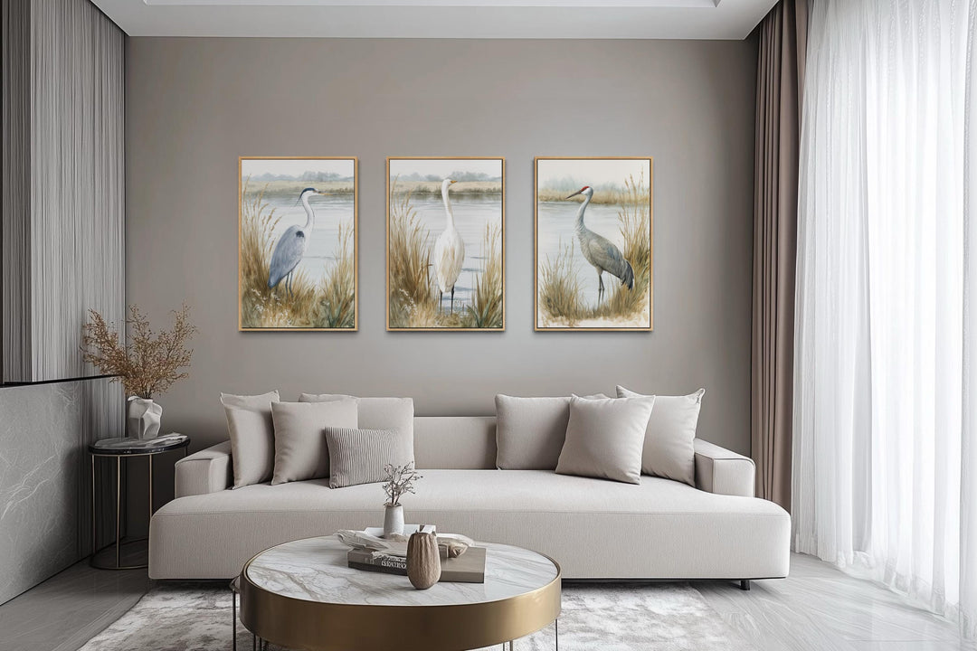 Three vertical canvas prints of a heron, egret, and crane in a neutral coastal living room.