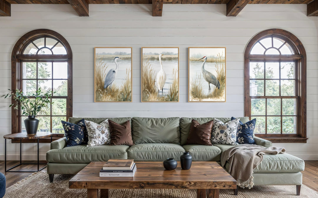A triptych of heron, egret, and crane prints in a neutral coastal style above a green sofa.