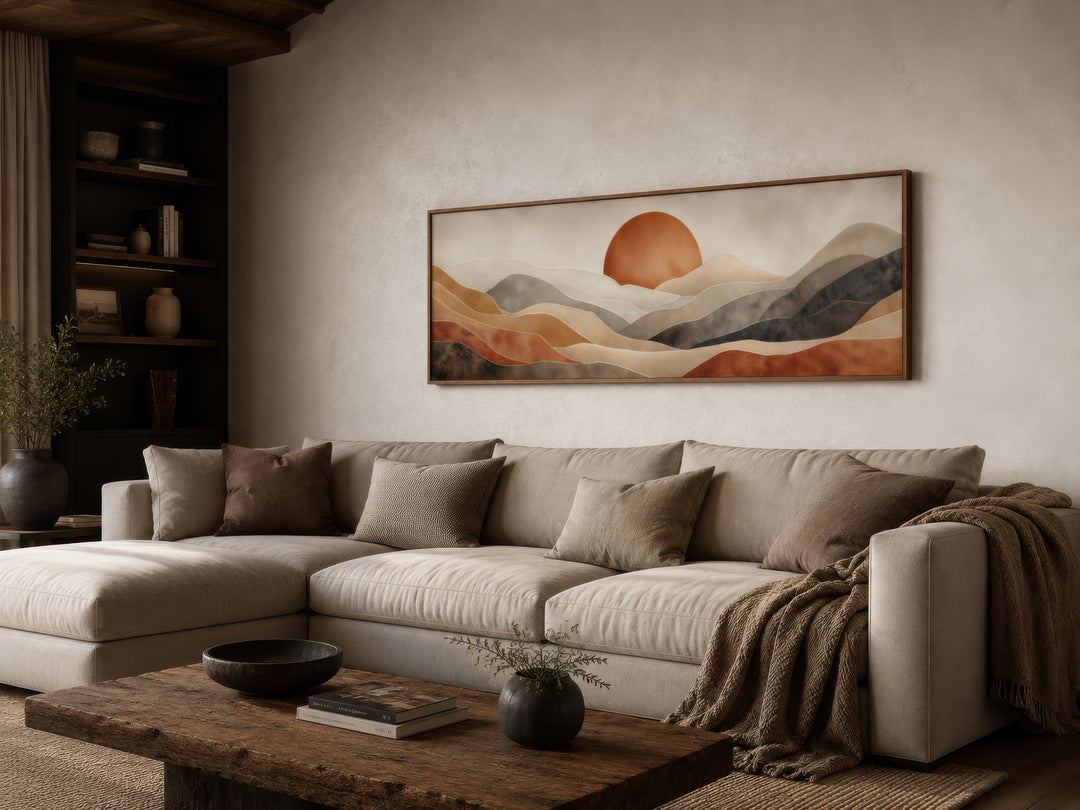 Boho desert wall art featuring a terracotta sun and rolling hills above a neutral sectional sofa.