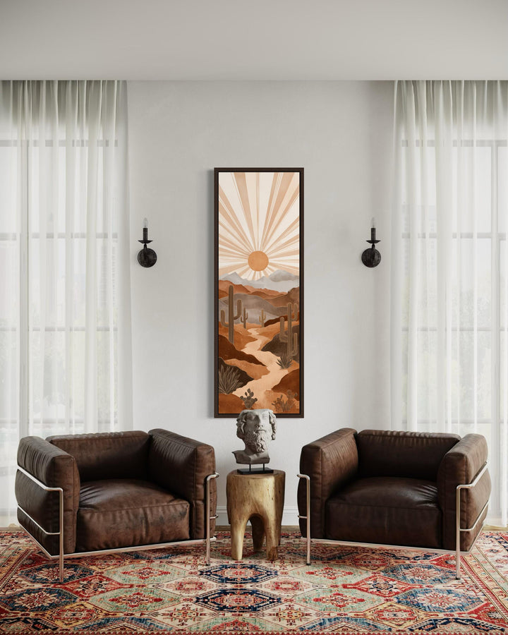 Tall narrow canvas art of a desert cactus landscape in terracotta tones above two leather chairs.