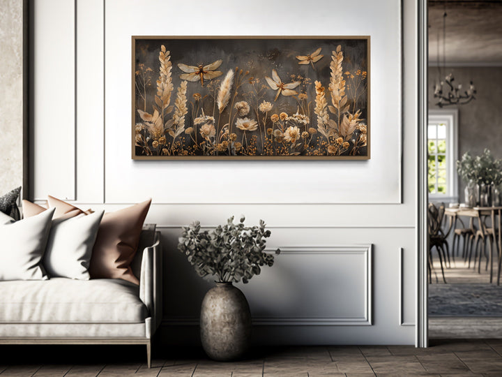Framed canvas wall art with dragonflies and grasses in brown and beige above a sofa.