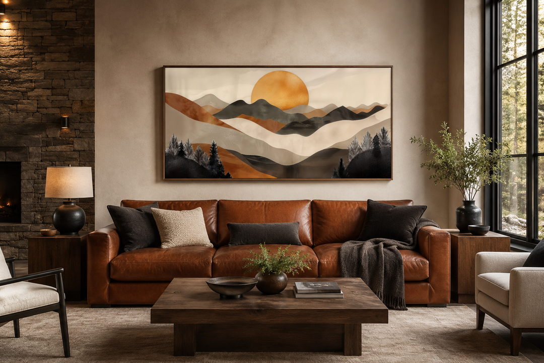 Boho mountain and sun framed canvas wall art in earth tones above a brown leather sofa.