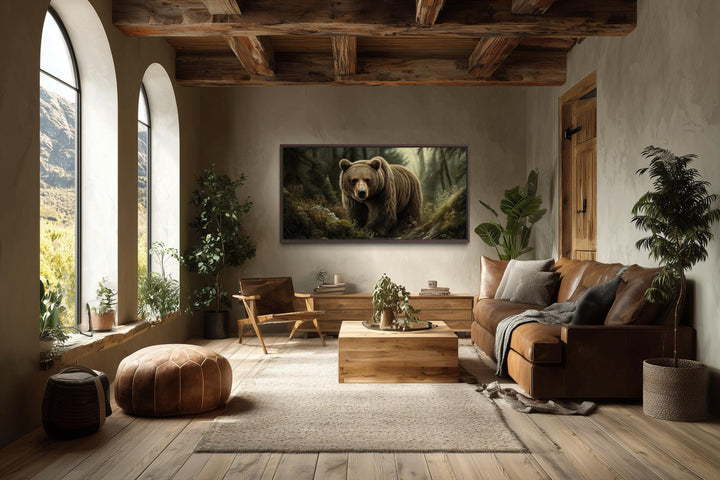 A framed canvas print of a brown bear in a forest hangs in a rustic living room with wood beams.