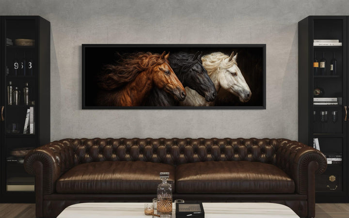 Large horizontal wall art featuring a portrait of brown, black, and white horses above a sofa.
