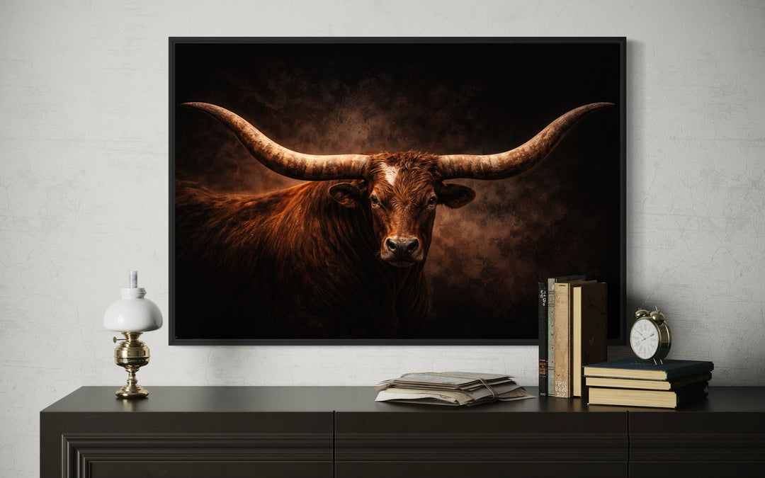 Brown longhorn bull canvas wall art in a black frame above a dark dresser with rustic decor.