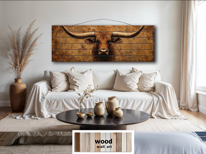 Brown longhorn steer printed on long narrow distressed wood planks hanging above a white sofa.