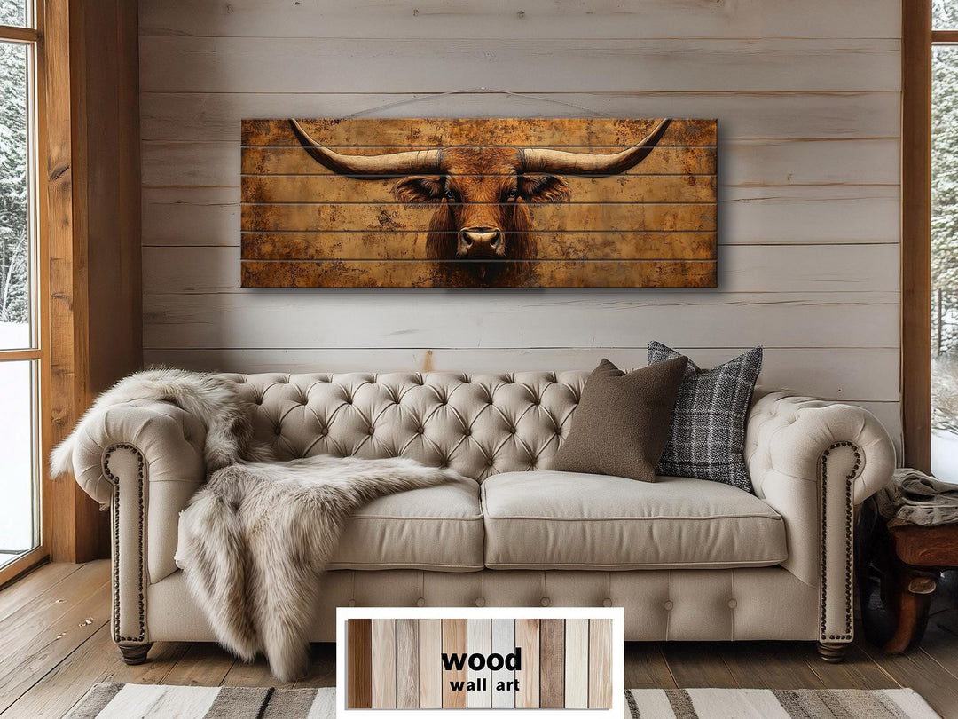 Long narrow wood wall art featuring a brown longhorn steer above a beige tufted sofa.