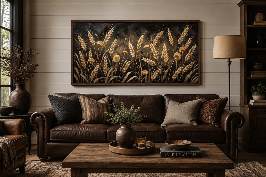 Framed horizontal canvas print of a boho wheat field in brown and beige above a leather sofa.