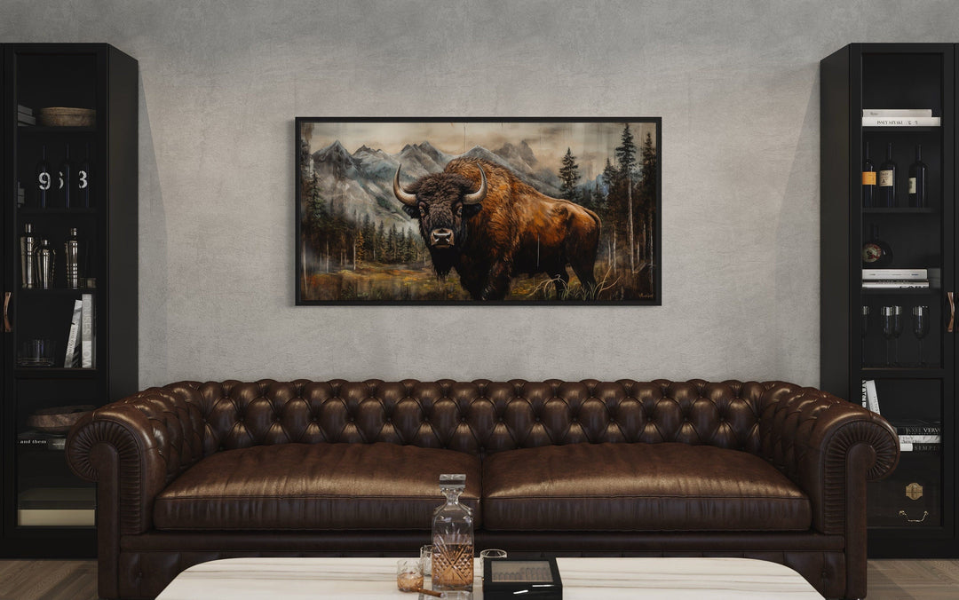 Rustic wood framed canvas of a buffalo in Yellowstone, hung above a brown leather sofa.