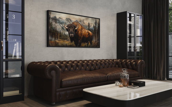 Rustic wood-framed canvas wall art of a buffalo in Yellowstone above a brown leather sofa.