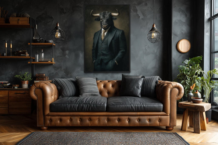 Framed canvas wall art of a bull in a dark suit hanging above a brown leather Chesterfield sofa.
