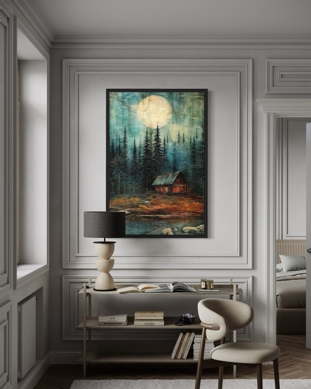 Framed canvas wall art of a cabin in a dark forest under a large moon, hanging in a modern room.