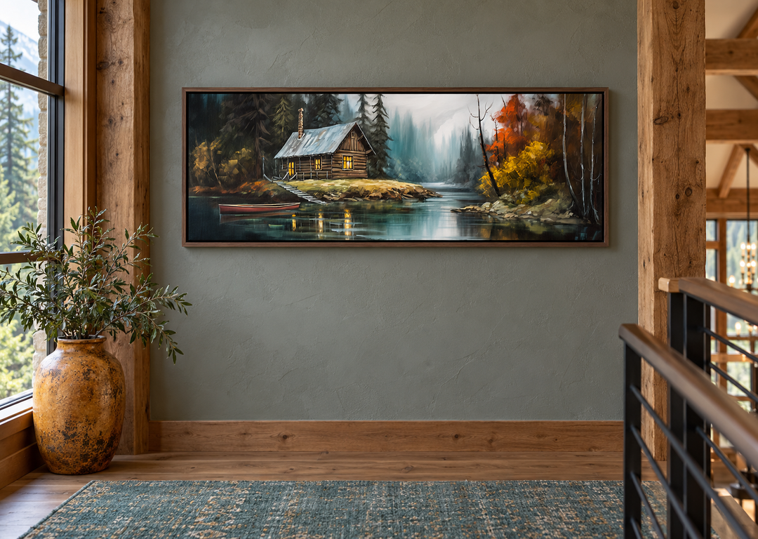 Narrow horizontal rustic framed canvas wall art of a cabin on a lake in a wooded landscape.