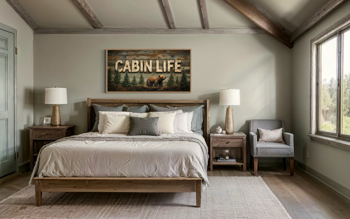 Cabin Life framed canvas wall art with a bear and fir trees hanging above a bed in a rustic bedroom.