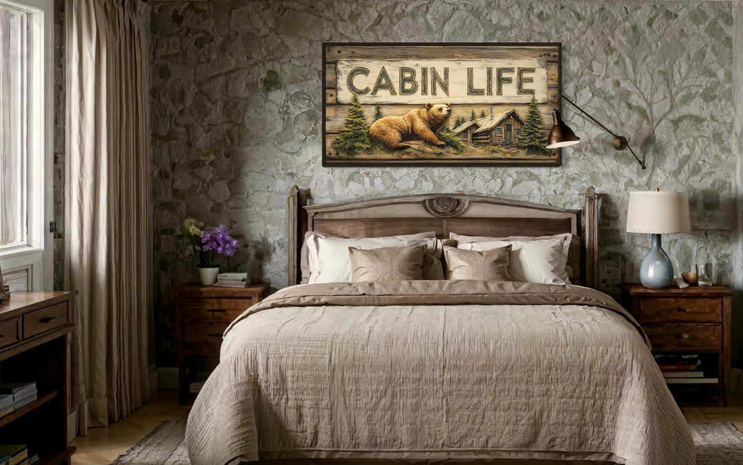 Cabin Life framed canvas wall art featuring a bear and log house above a bed in a rustic room.
