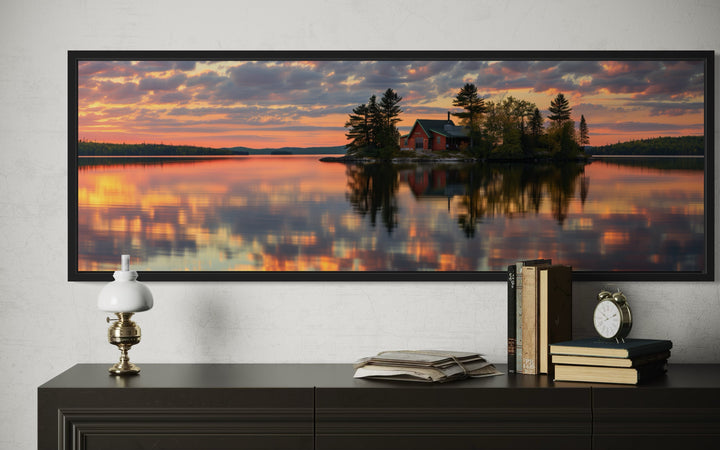Panoramic framed canvas art of a red cabin on a lake at sunset, displayed above a dark dresser.
