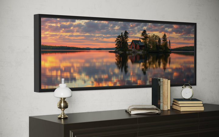 Panoramic framed canvas art of a cabin on a lake at sunset, displayed above a dark wood dresser.