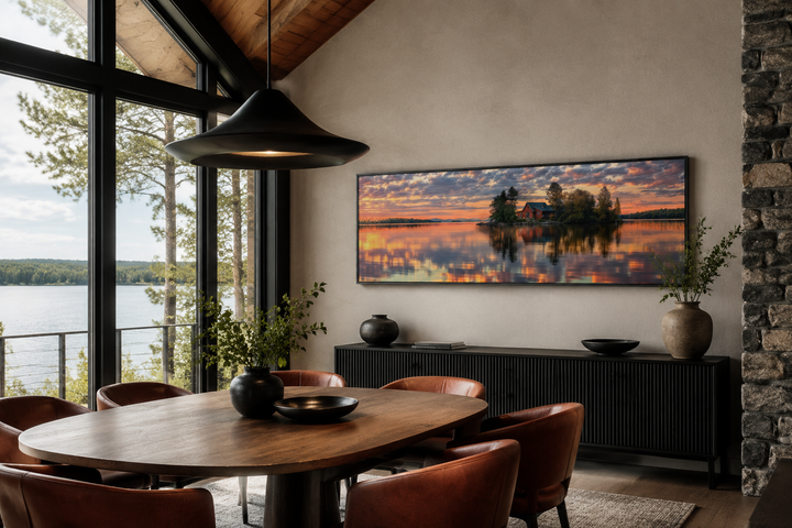 Long horizontal framed canvas wall art of a cabin on a lake at sunset in a modern dining room.