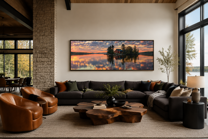 Long horizontal framed canvas wall art of a cabin on a lake at sunset in a modern living room.