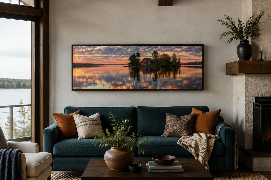 Long horizontal framed canvas wall art of a cabin on a lake at sunset above a teal sofa.