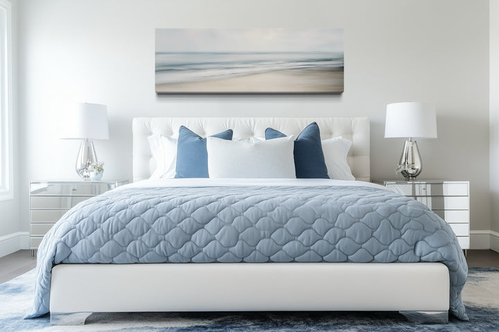 Calm long horizontal ocean framed canvas wall art hanging above a white tufted bed.
