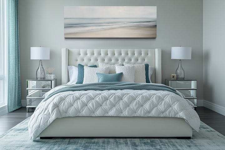 Calm long horizontal ocean framed canvas wall art hanging above a bed in a coastal bedroom.