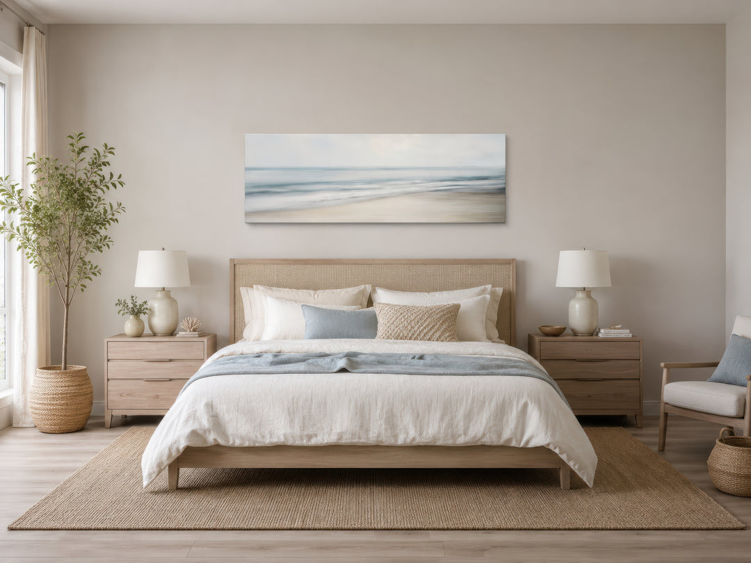 Calm long horizontal ocean framed canvas wall art above a bed in a coastal-style bedroom.