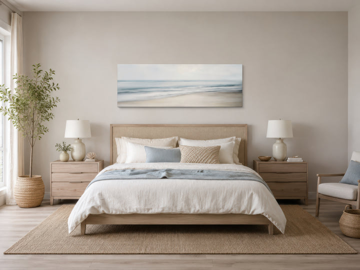 Calm long horizontal ocean framed canvas wall art above a bed in a coastal-style bedroom.