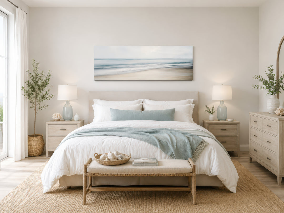 Calm long horizontal ocean framed canvas wall art hanging above a bed in a coastal bedroom.