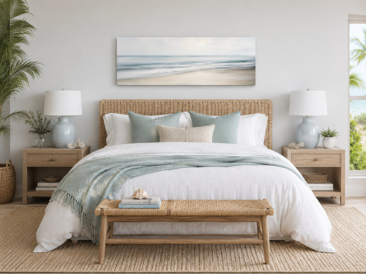 Long horizontal framed canvas wall art of a calm ocean beach scene hanging above a bed.