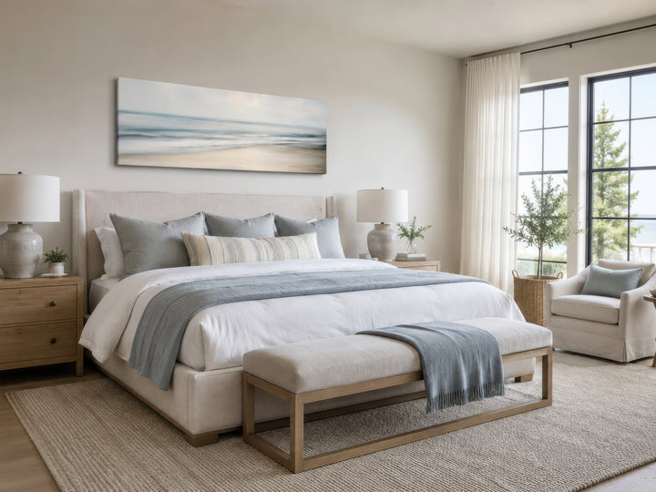 Calm long horizontal ocean framed canvas wall art hanging above a bed in a coastal bedroom.