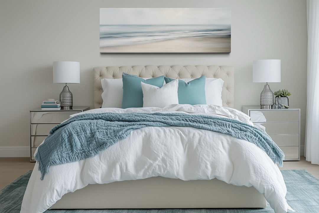 Horizontal framed canvas wall art of a calm ocean scene hanging above a bed in a neutral bedroom.