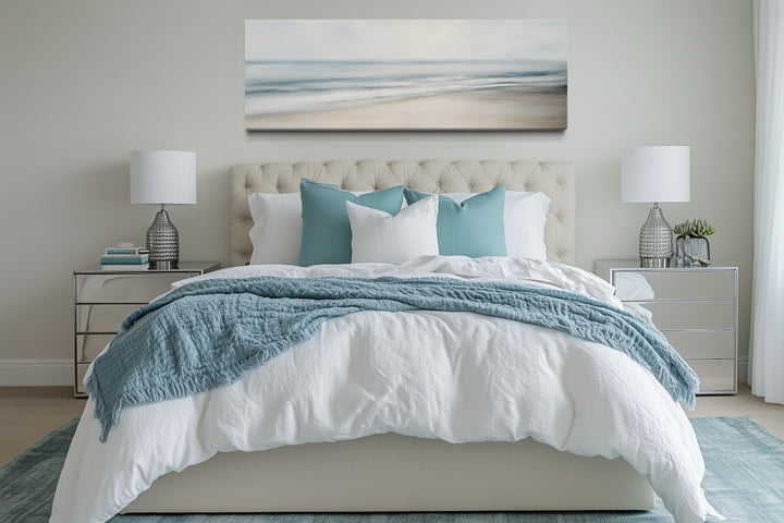 Horizontal framed canvas wall art of a calm ocean scene hanging above a bed in a neutral bedroom.