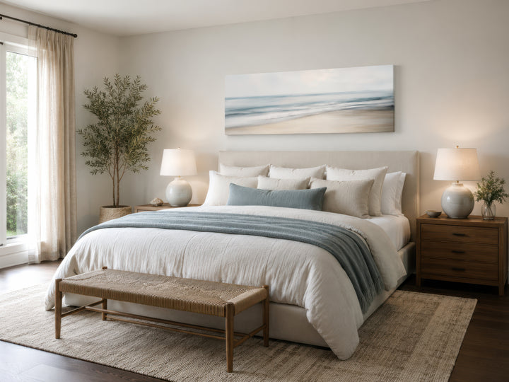 Calm long horizontal ocean framed canvas wall art above a bed in a serene coastal bedroom.