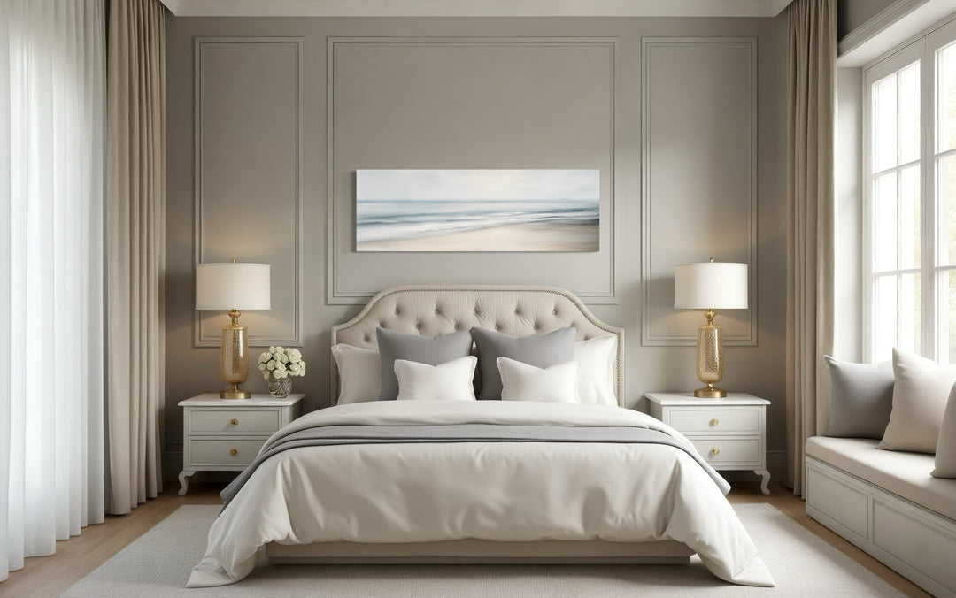 Calm long horizontal ocean framed canvas wall art hanging above a bed in a neutral bedroom.