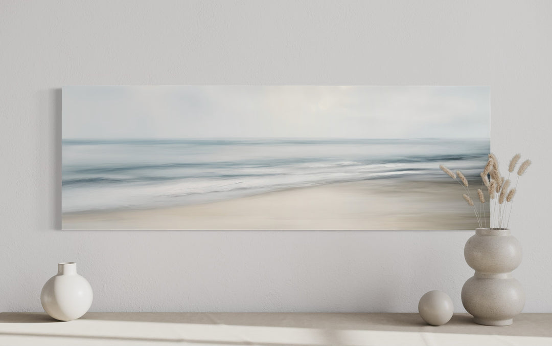 Calm long horizontal ocean framed canvas wall art with soft blue and gray waves on a white wall.