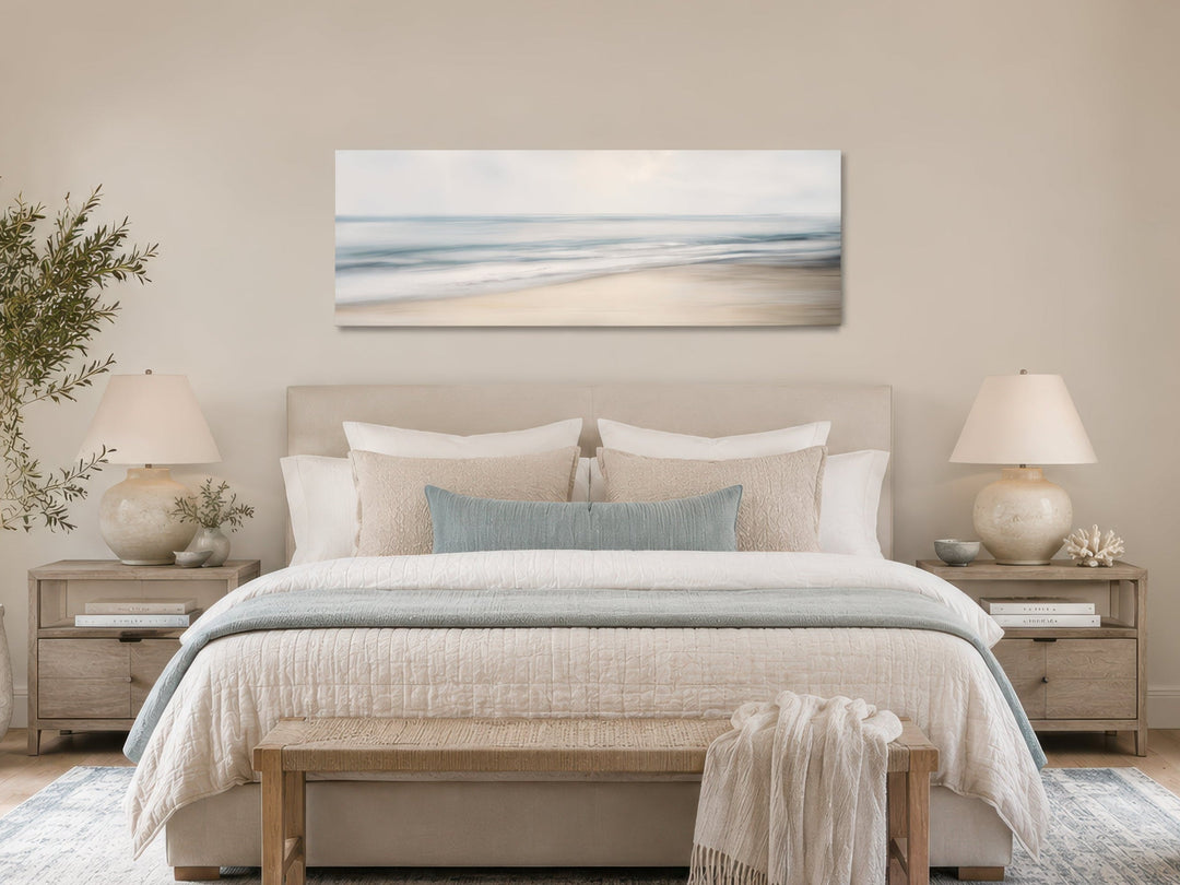 Calm long horizontal ocean framed canvas wall art hanging above a bed in a neutral-toned bedroom.