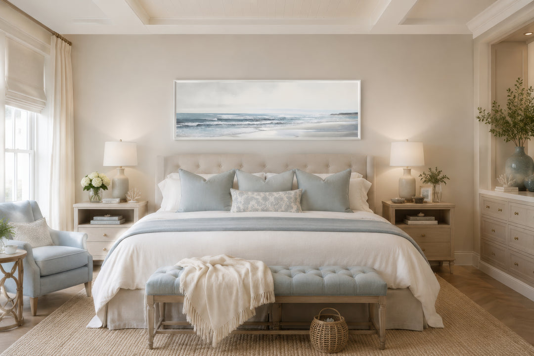 A long horizontal framed canvas featuring a minimalist coastal landscape above a bed.