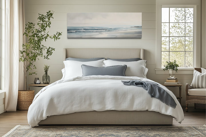 Long horizontal framed canvas wall art featuring a minimalist coastal beach scene above a bed.
