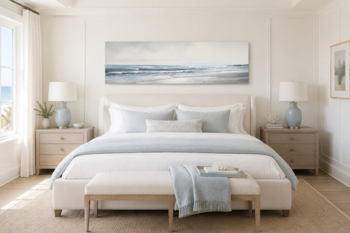 A long horizontal framed canvas of a minimalist beach landscape hangs above a neutral-toned bed.