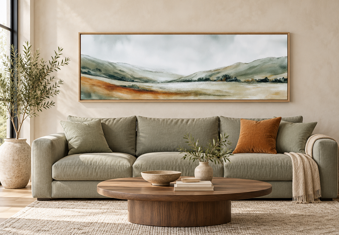 Panoramic green landscape canvas print in a wood frame above a sage sofa in a minimalist room.