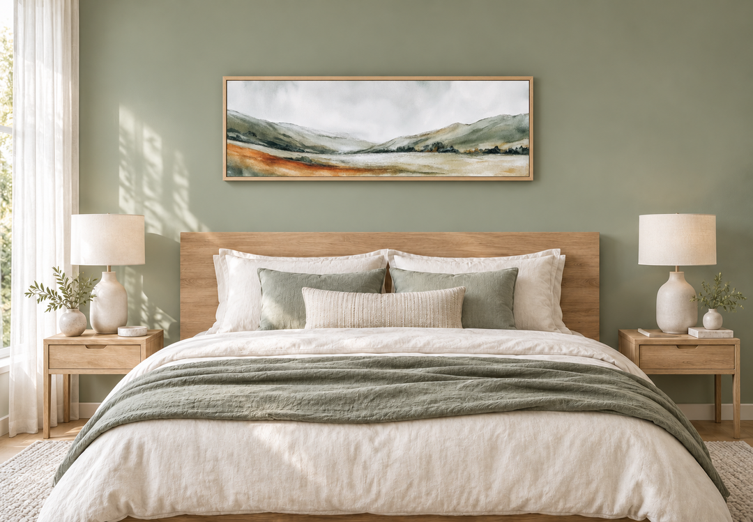 Panoramic green landscape canvas print in a light wood frame above a bed in a sage green bedroom.