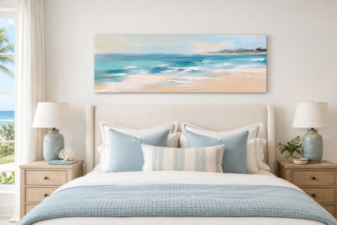 Panoramic coastal canvas wall art of a calm ocean beach hanging above a bed in a neutral bedroom.