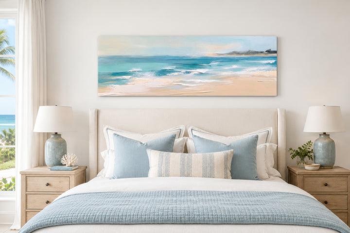 Panoramic coastal canvas wall art of a calm ocean beach hanging above a bed in a neutral bedroom.
