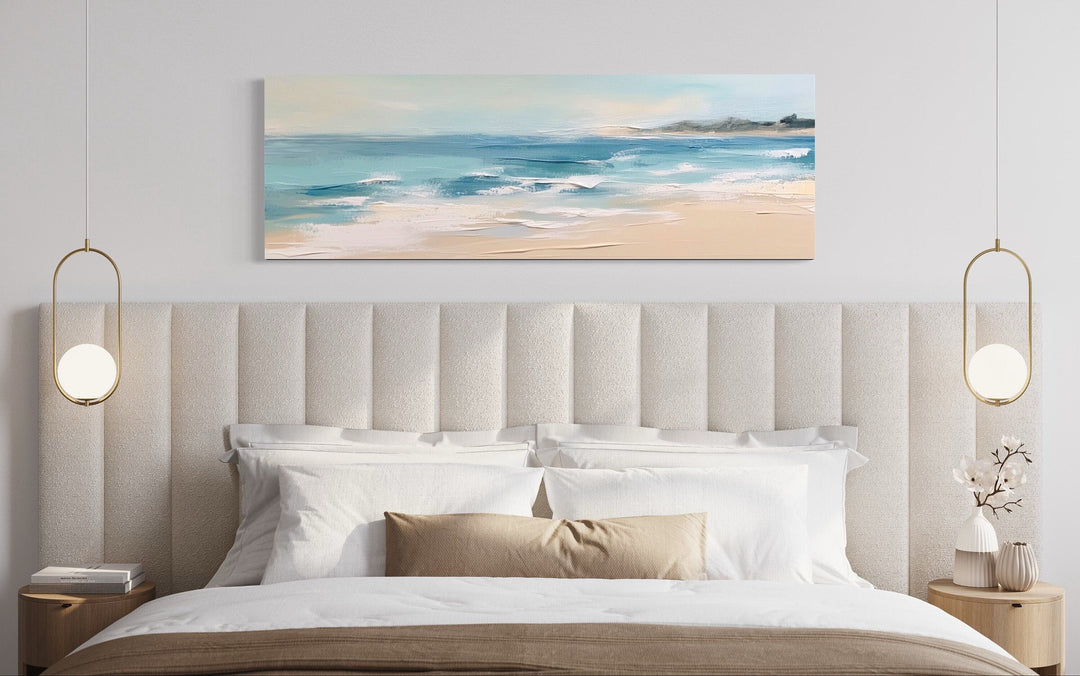 Panoramic coastal canvas wall art of a calm ocean beach hanging over a bed in a modern bedroom.