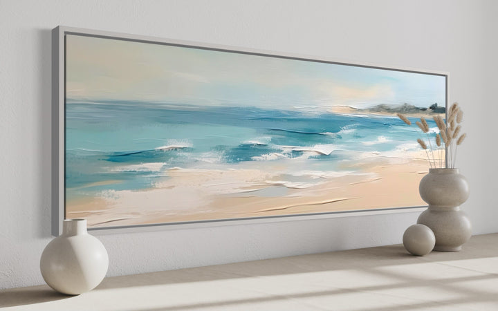 Panoramic framed canvas wall art of a calm ocean beach with aqua waves and neutral beige sand.