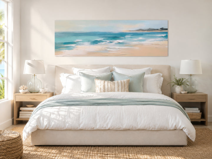 Panoramic coastal canvas wall art of a calm ocean beach hanging above a bed in a neutral bedroom.