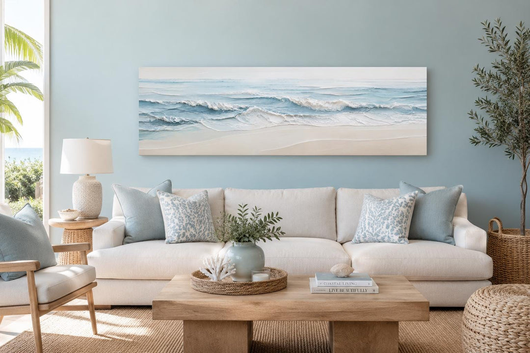 Wide horizontal canvas of calm ocean waves in soft blue and cream tones above a white sofa.