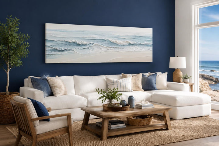 Wide horizontal canvas print of calm ocean waves in blue and cream tones above a white sofa.