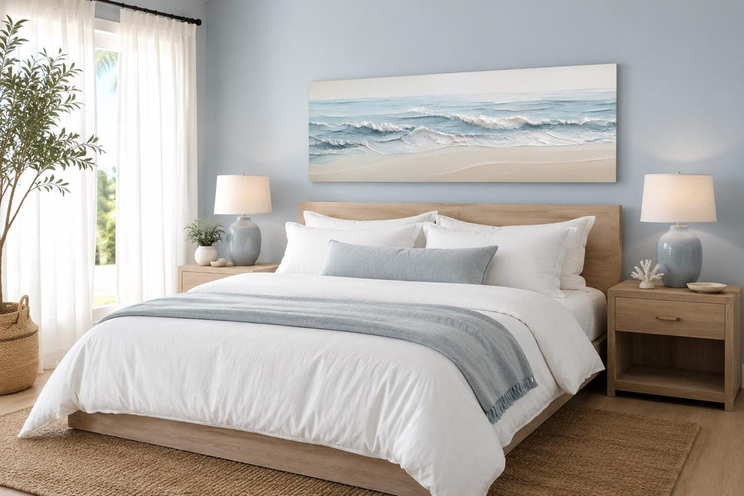 Wide horizontal canvas print of soft blue ocean waves on a sandy beach above a bed.
